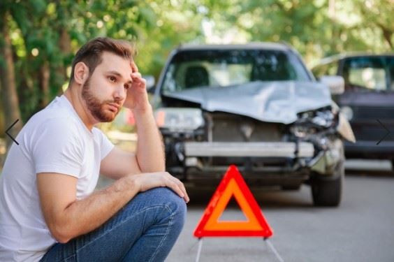 man sitting on the side of the road after car accident